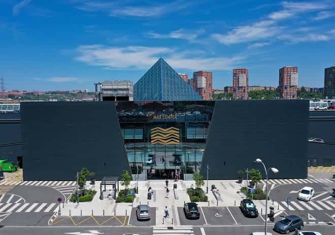 Plaza principal frente al Max Center con pirámide de cristal y acceso peatonal