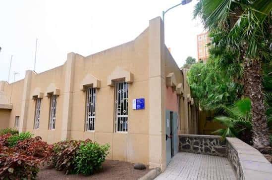 Vista exterior de la Biblioteca Pública Municipal San Juan con fachada amarilla y palmeras