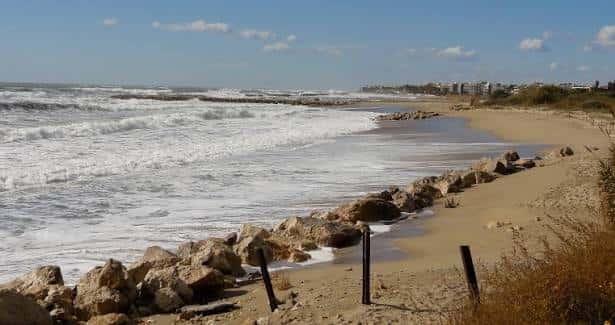 Vista panorámica de la playa con olas rompiendo y rompeolas de piedra