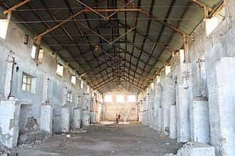 Interior del antiguo galpón industrial con estructura metálica y muros deteriorados