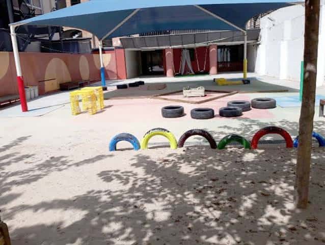 Patio exterior con zona de juegos, neumáticos pintados y sombra azul