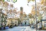 Plaza arbolada con bancos y la torre de la iglesia visible a lo lejos