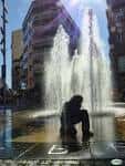 Escultura de un niño en la fuente con chorros de agua verticales al fondo