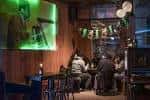 Zona de asientos del pub con mesas, sillas y una pantalla proyectando contenido