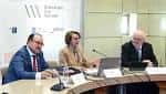 Panel de ponentes en una mesa de conferencias con fondo de pared texturizada