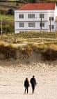 Dos personas caminando por la arena de la Playa de Barrañán con un edificio al fondo