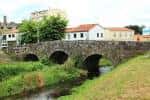Antiguo puente de piedra sobre el río Sar con casas tradicionales al fondo