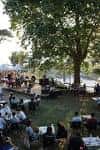 Zona de eventos al aire libre bajo los árboles con mesas y asistentes