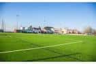 Campo de fútbol de césped artificial con gradas y edificios al fondo