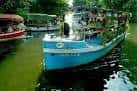 Barcos con asistentes navegando por el río durante la Romaría de Os Caneiros
