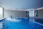 Piscina interior de un spa con chorros de agua y grandes ventanales.