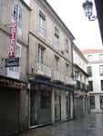 Edificio de piedra con balcones y comercios en una calle de Ourense