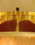 Interior de sala de eventos con butacas rojas y escenario