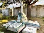 Tumba con cruz y escultura de ángel en un entorno arbolado