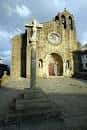 Fachada principal de la iglesia con un crucero de piedra en la plaza.