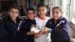 Cuatro estudiantes sonrientes mostrando un proyecto de ciencia en el aula