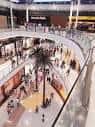 Perspectiva interior desde un nivel superior del centro comercial con palmeras y visitantes.