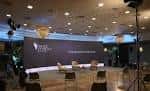 Escenario de evento con gran pantalla LED y asientos para ponentes