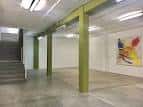 Amplio salón de MUTA con pilares verdes y escalera