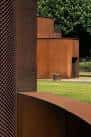Primer plano de la fachada perforada de acero corten y una pared curva