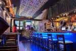 Interior de bar Jukebox en Vigo con barra iluminada en azul y asientos