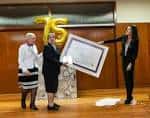 Ceremonia de aniversario con tres adultos y un globo con el número 75
