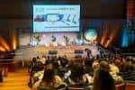 Interior del auditorio con panel de ponentes en el escenario y público asistente
