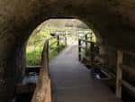 Pasarela de madera saliendo de un túnel de piedra en el paseo fluvial