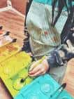 Persona pintando con delantal y paleta en un taller de expresión
