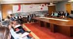Amplia sala de reuniones con asistentes sentados en una mesa ovalada