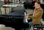 Hombre tocando un piano de cola en el showroom de instrumentos
