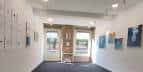 Interior de galería de arte con obras expuestas y entrada luminosa