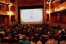 Interior de una sala de cine con público y pantalla proyectando