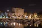 Muelle de Curuxeiras iluminado por la noche con reflejos en el agua y edificios al fondo