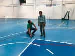 Pista de baloncesto interior con dos personas inspeccionando el suelo