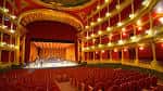 Interior de un teatro clásico con butacas rojas y palcos
