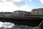 Panorámica de la Praza de Valentín García Escudero junto al río con edificios reflejados en el agua.