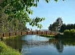 Puente de madera sobre el agua tranquila rodeado de árboles en A Xunqueira de Alba