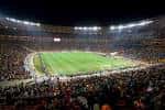 Estadio de fútbol iluminado por la noche con público en las gradas