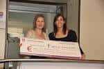 Dos mujeres presentando un cheque de donación en un evento benéfico.