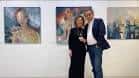 Dos personas posando frente a obras de arte en una exposición