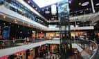 Pasillo interior del Centro Comercial As Cancelas con escaleras mecánicas y tiendas.