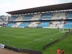 Vista del estadio de fútbol con gradas azules y blancas y el campo de juego
