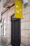 Entrada principal de MUTA con cartel amarillo en fachada de piedra