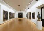 Sala de exposición interior del museo con obras de arte y suelo de madera