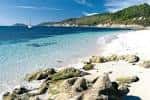 Playa de arena blanca y aguas cristalinas con un velero al fondo