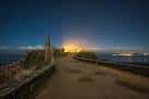 Vista nocturna del camino y las ruinas de A Lanzada con luces distantes