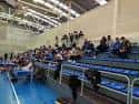 Interior de las gradas del polideportivo con asientos azules y vista parcial de la pista