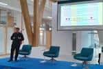 Ponente en un escenario moderno con pantalla y asientos durante un evento