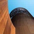 Perspectiva ascendente de una torre cilíndrica de acero corten bajo cielo azul